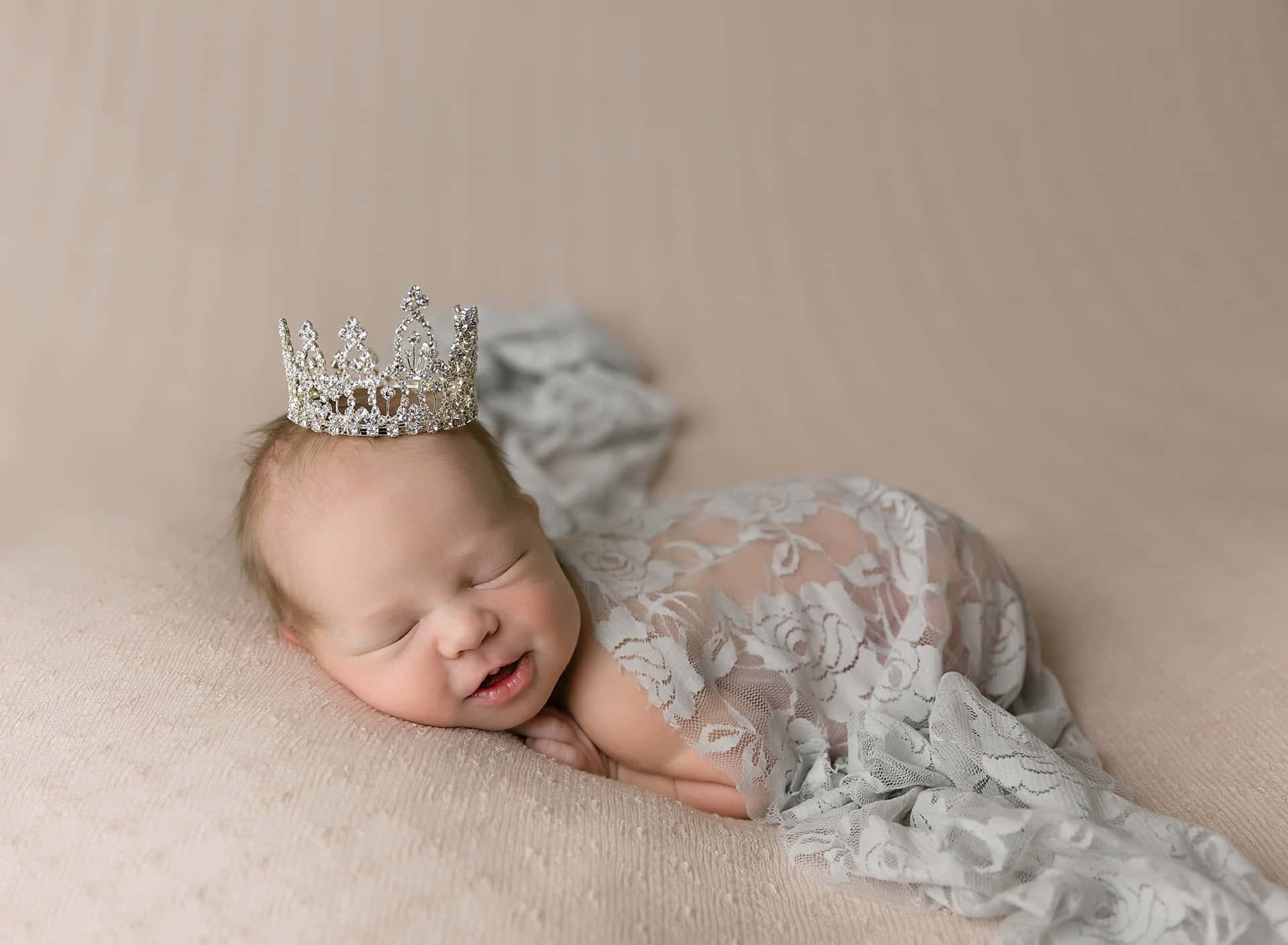 A Baby Girl Wearing A Tiara While Laying On A Blanket Background