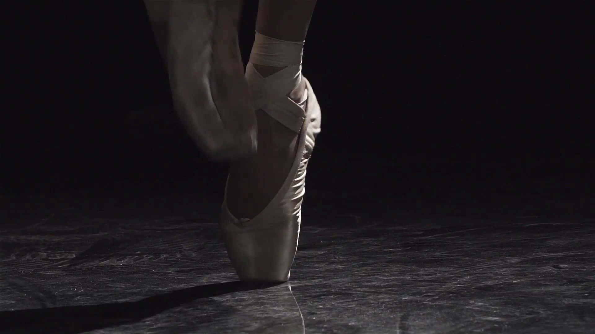 A Ballet Dancer Is Standing On A Dark Floor Background
