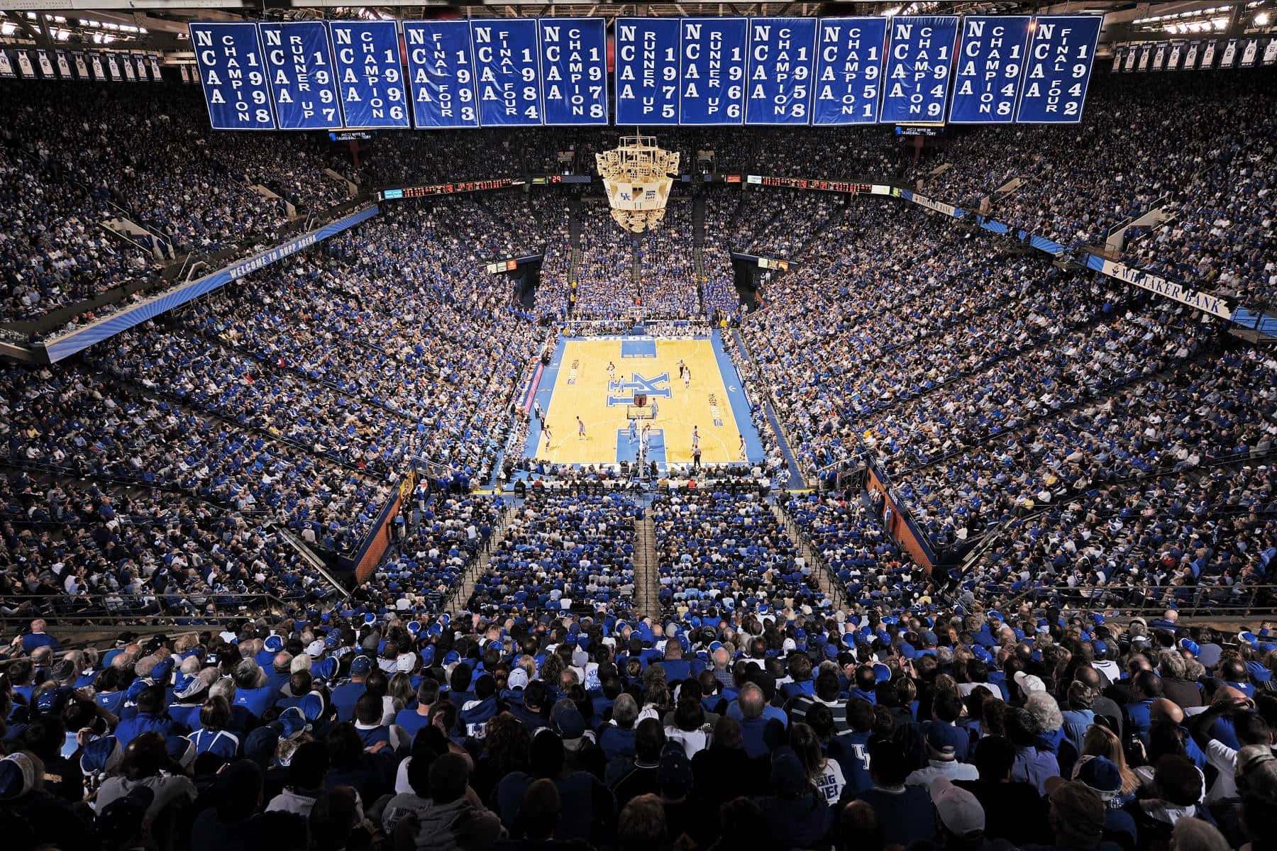 A Basketball Game In A Large Arena With Blue And White Fans Background