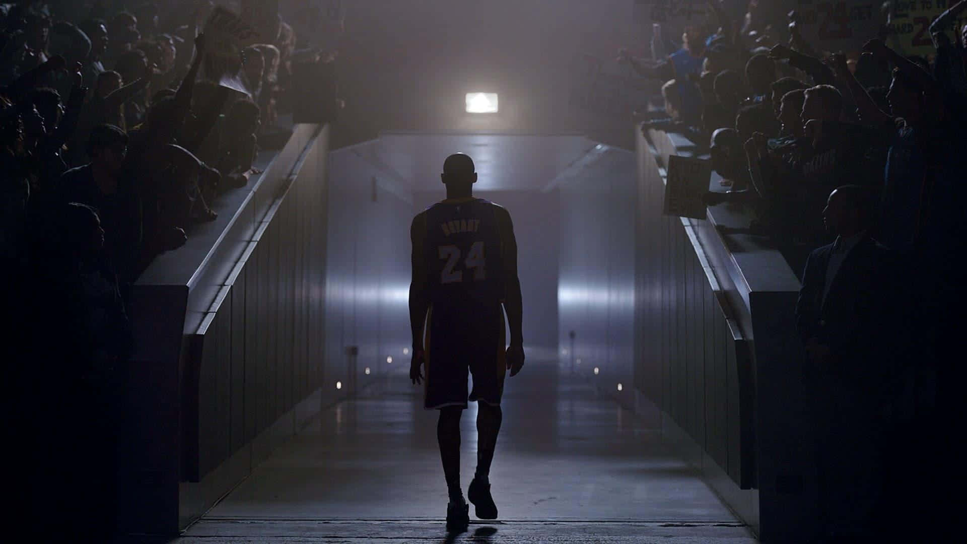 A Basketball Player Walks Down A Hallway With A Crowd Background