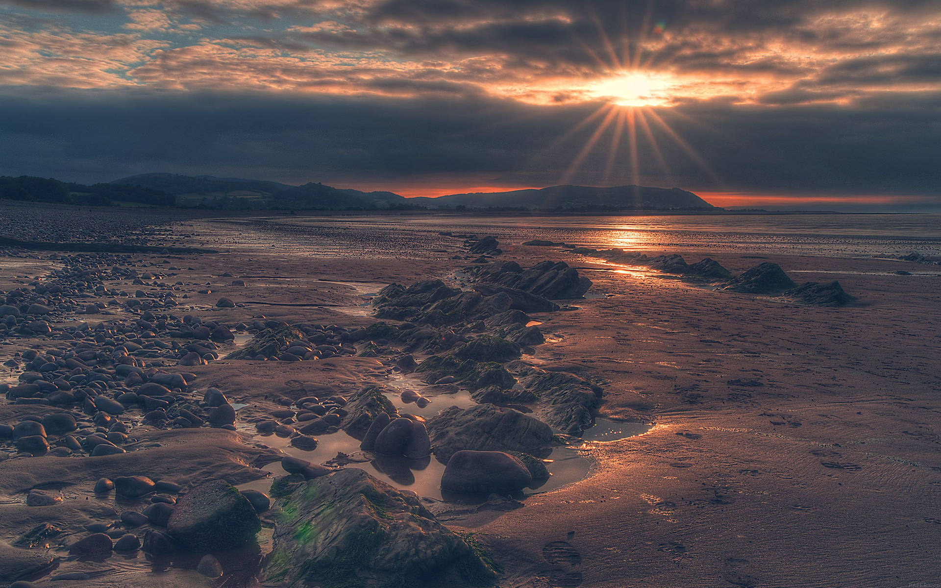 A Beach With Rocks And A Sun Setting Behind It