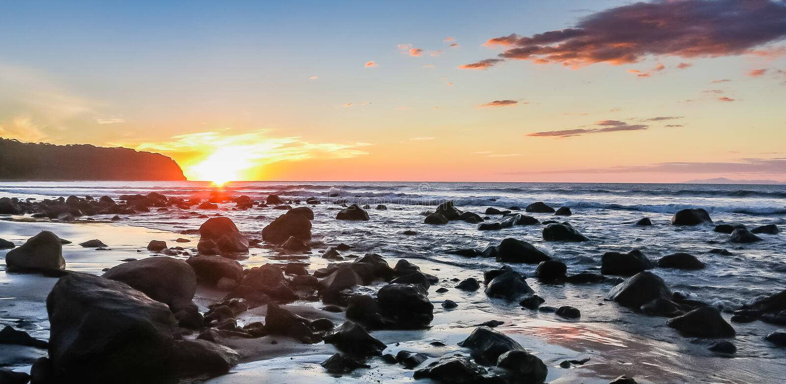 A Beach With Rocks And A Sunset Background