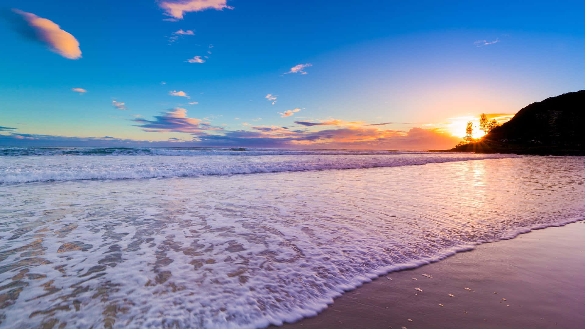 A Beach With Waves And A Cliff At Sunset