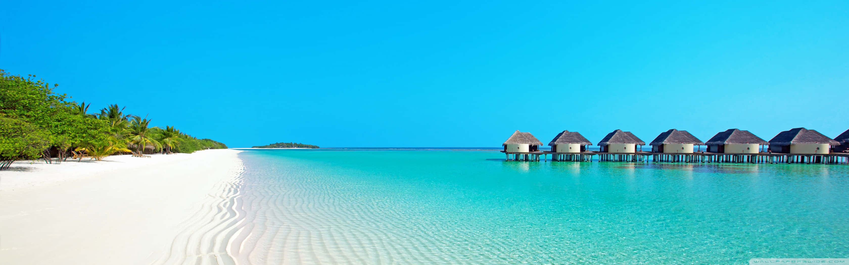 A Beach With White Huts And Clear Water Background