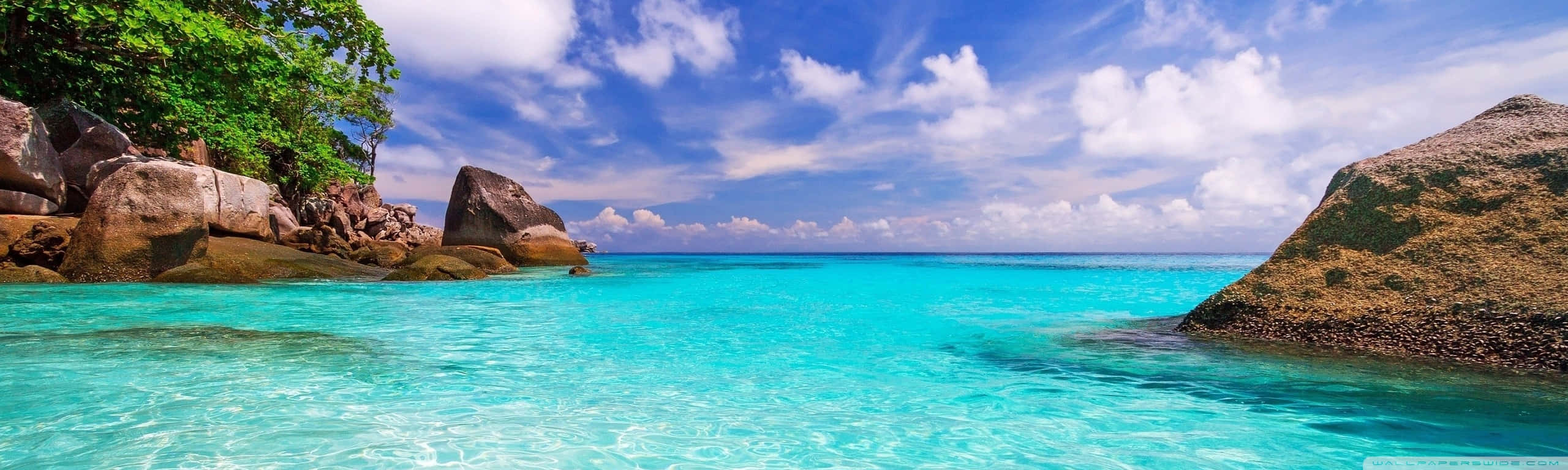 A Beautiful Blue Ocean With Rocks And Trees Background
