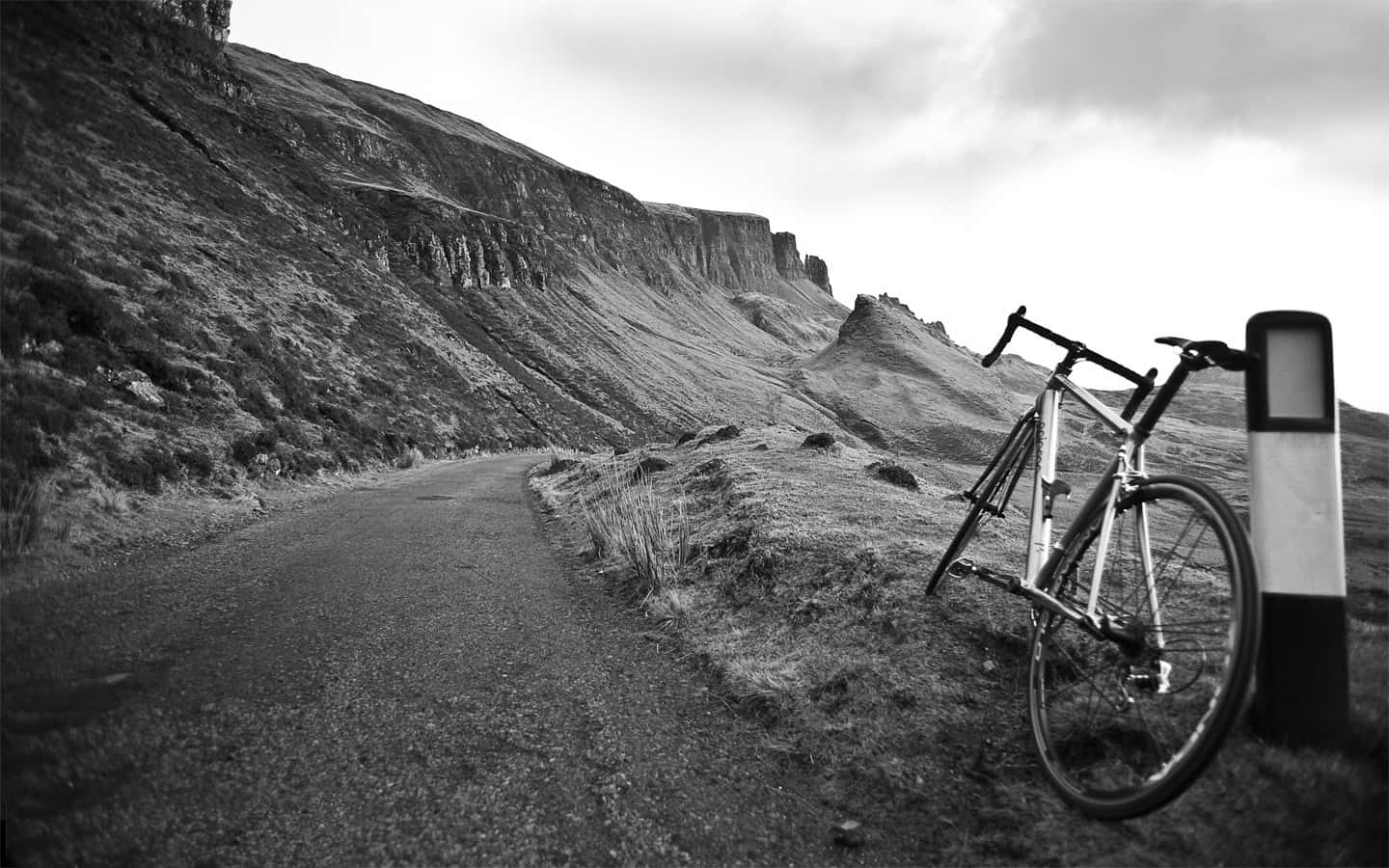 A Bicycle Leaning Against A Pole On A Mountain Road Background