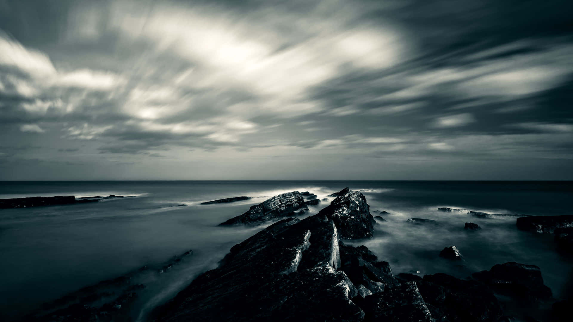 A Black And White Image Of A Rocky Shore With Clouds Background