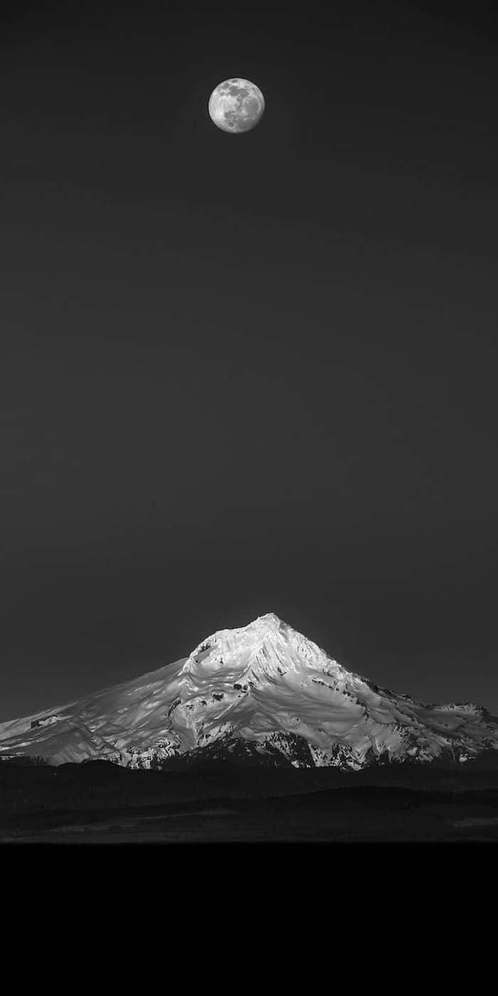 A Black And White Photo Of A Mountain With A Moon In The Sky Background