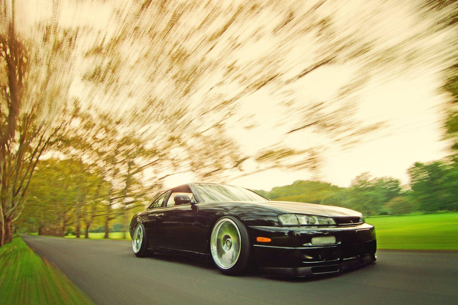 A Black Car Driving Down A Road With Blurred Motion Background