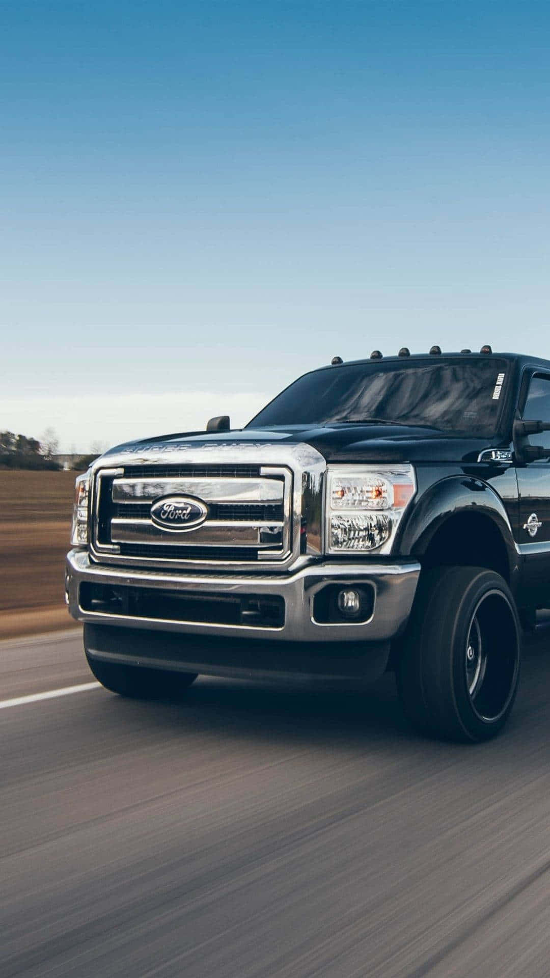A Black Ford Super Duty Truck Is Driving Down The Road Background