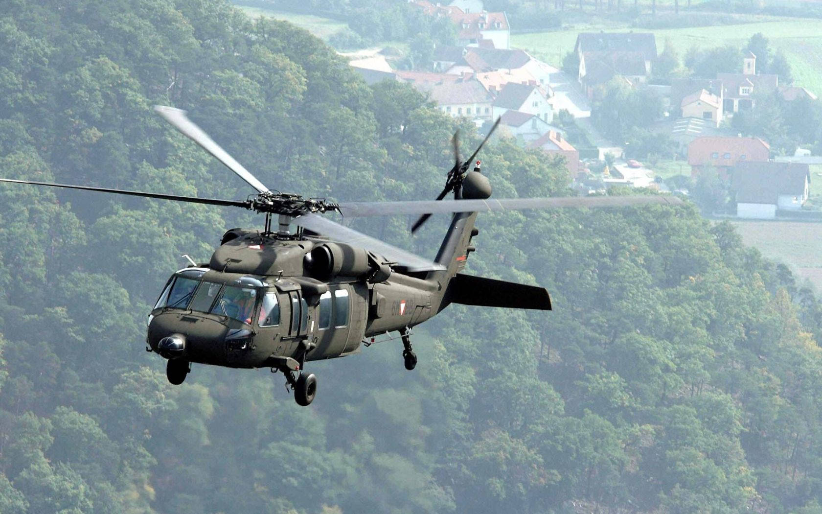 A Black Helicopter Flying Over A Forest Background