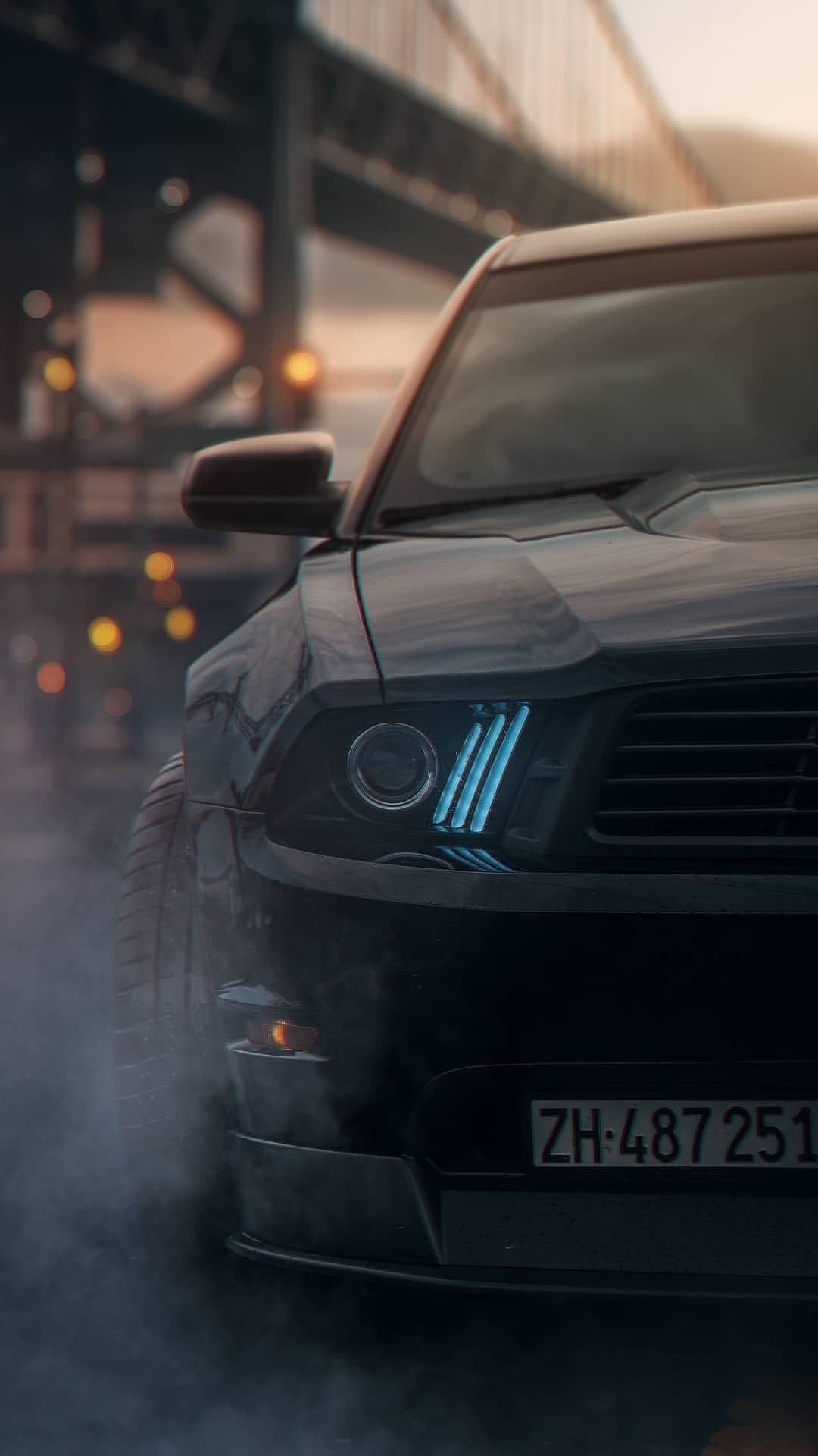 A Black Mustang Parked On A Street With Smoke Coming Out Of It Background