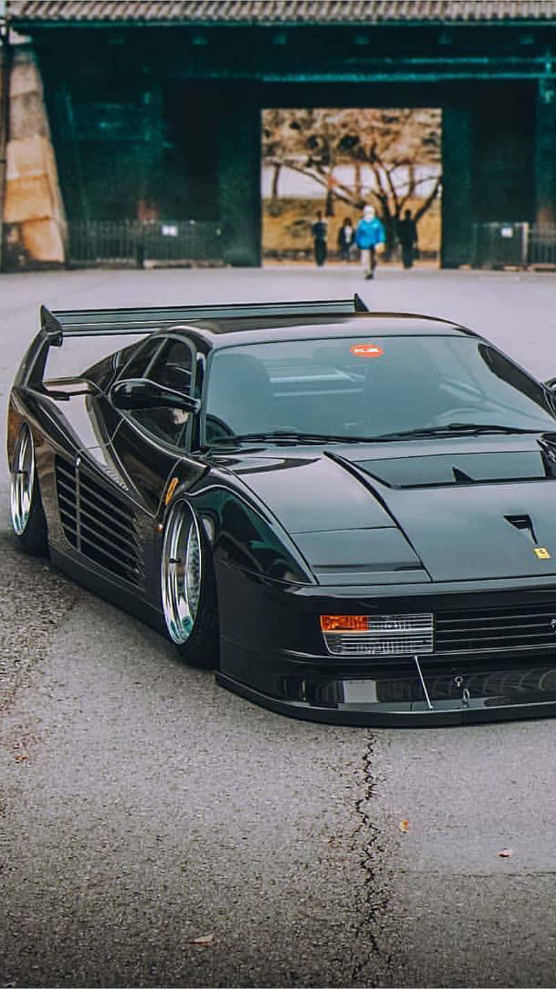 A Black Sports Car Parked In Front Of A Building Background