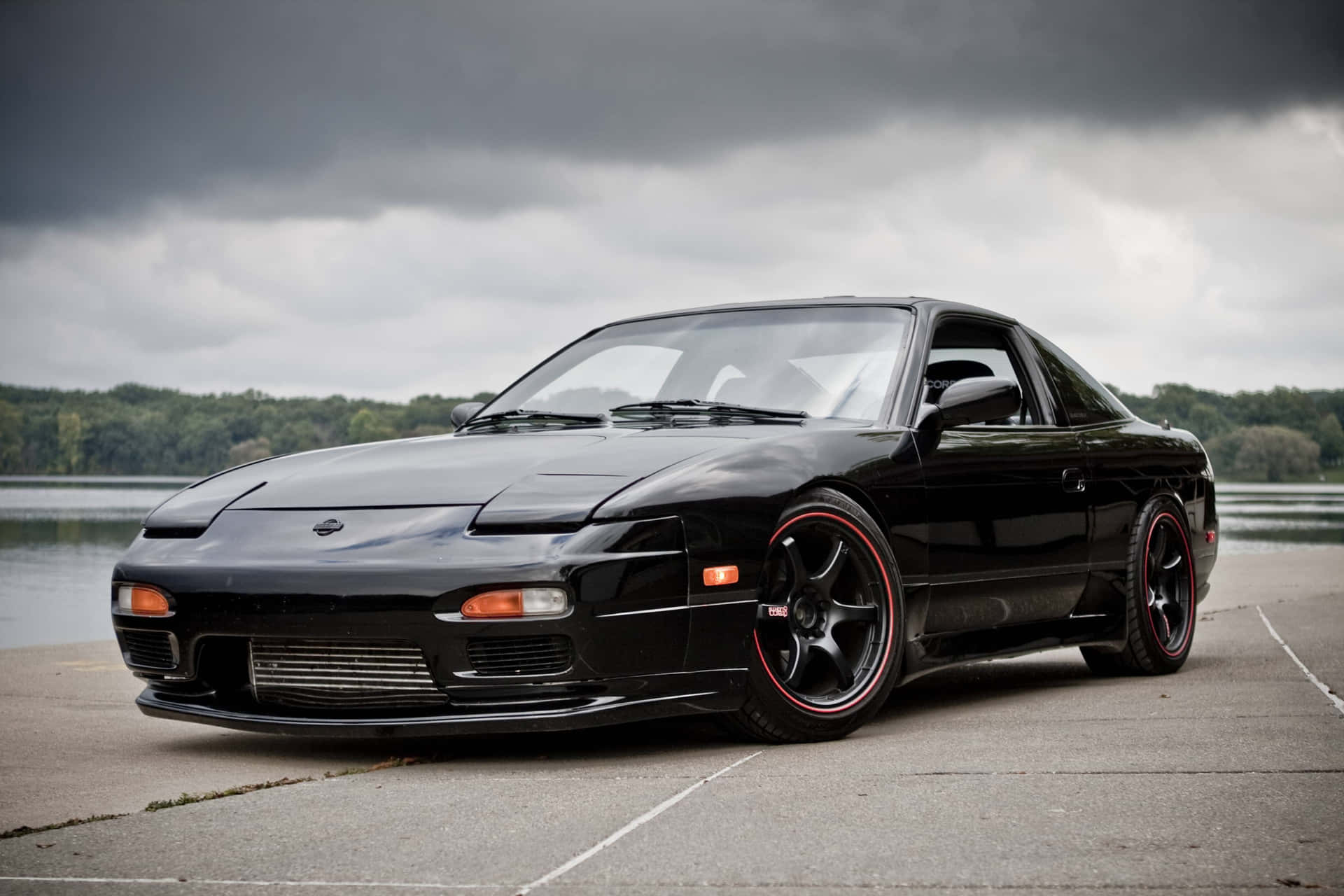 A Black Sports Car Parked In Front Of A Lake Background