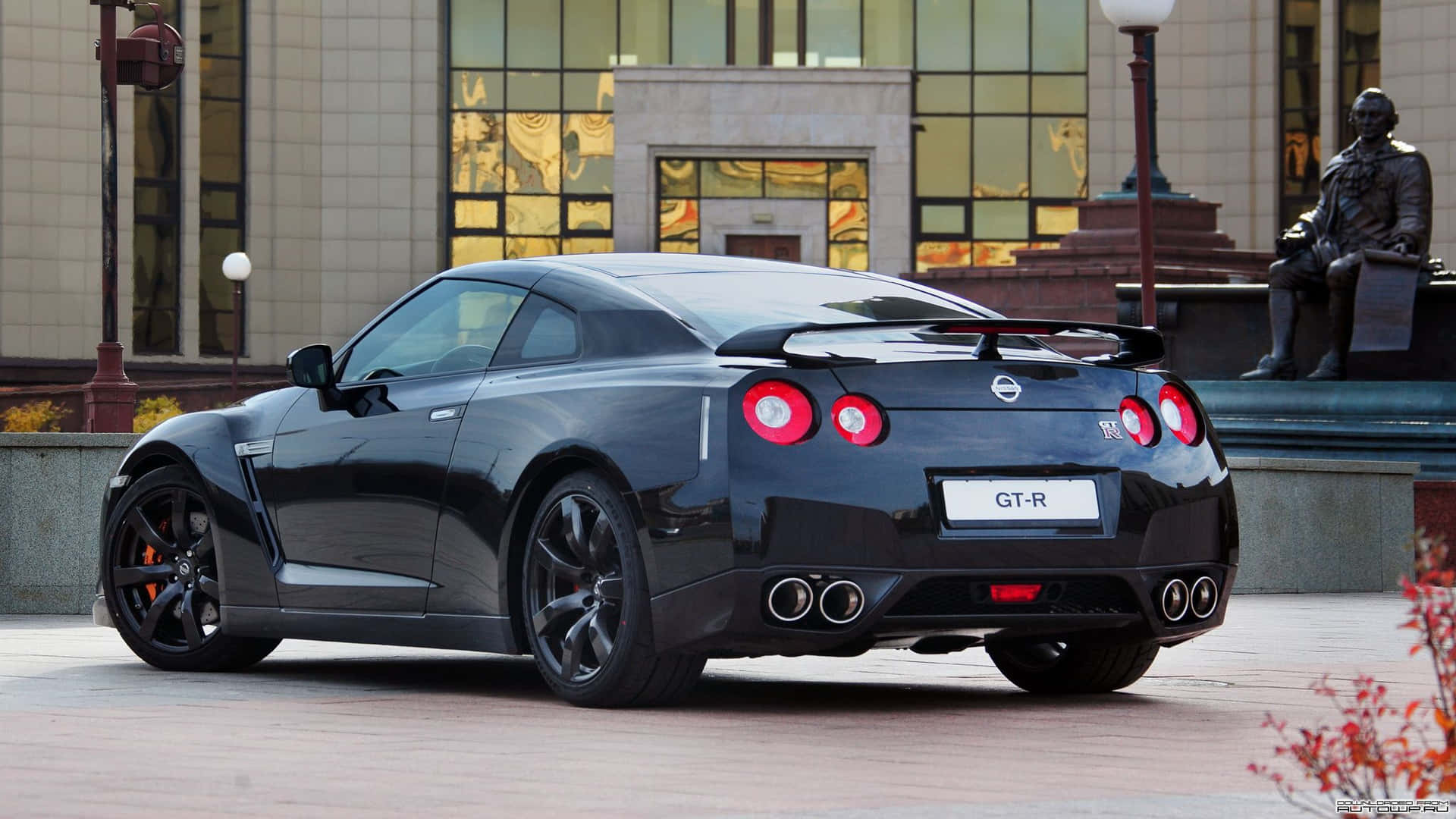 A Black Sports Car Parked In Front Of A Statue Background