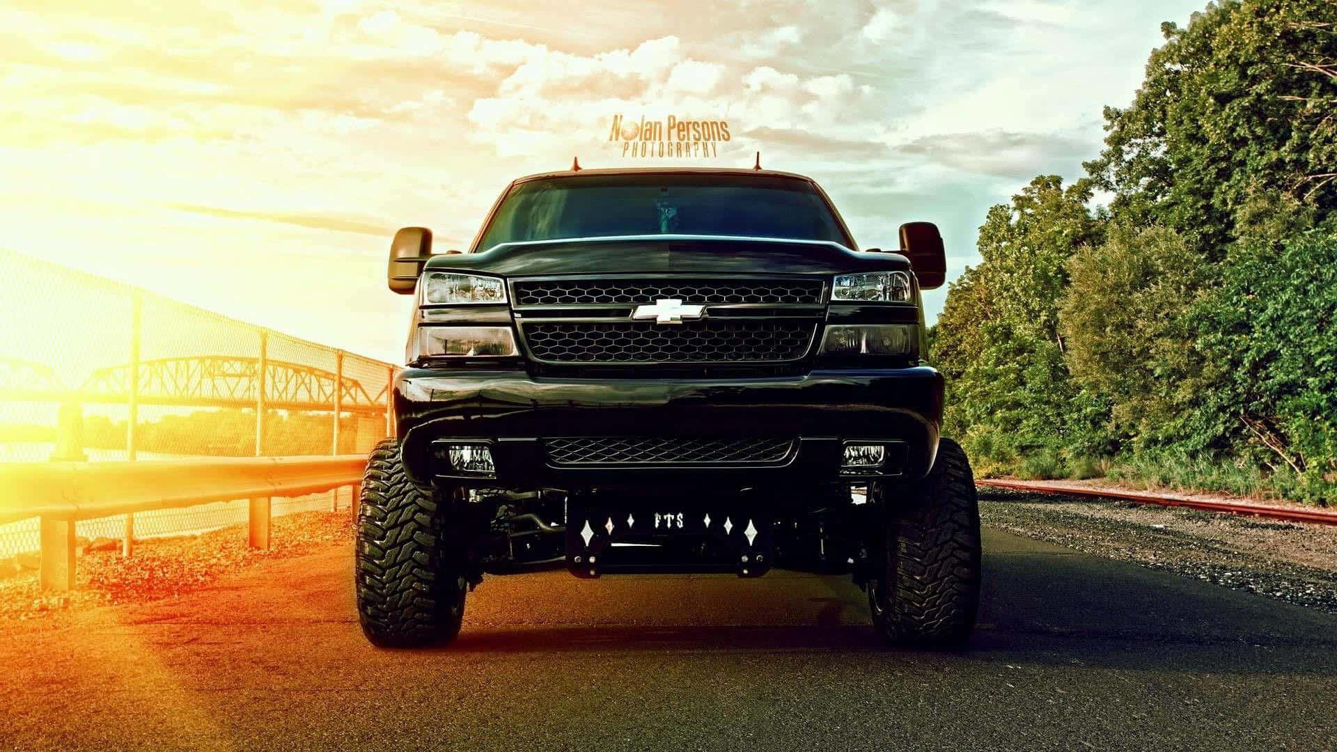 A Black Truck Driving Down A Road At Sunset Background