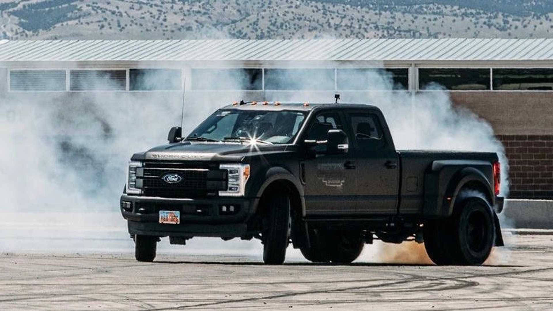 A Black Truck Is Driving Down A Track With Smoke Coming Out Of It Background