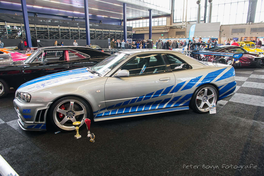 A Blue And Silver Car Is On Display At A Show Background