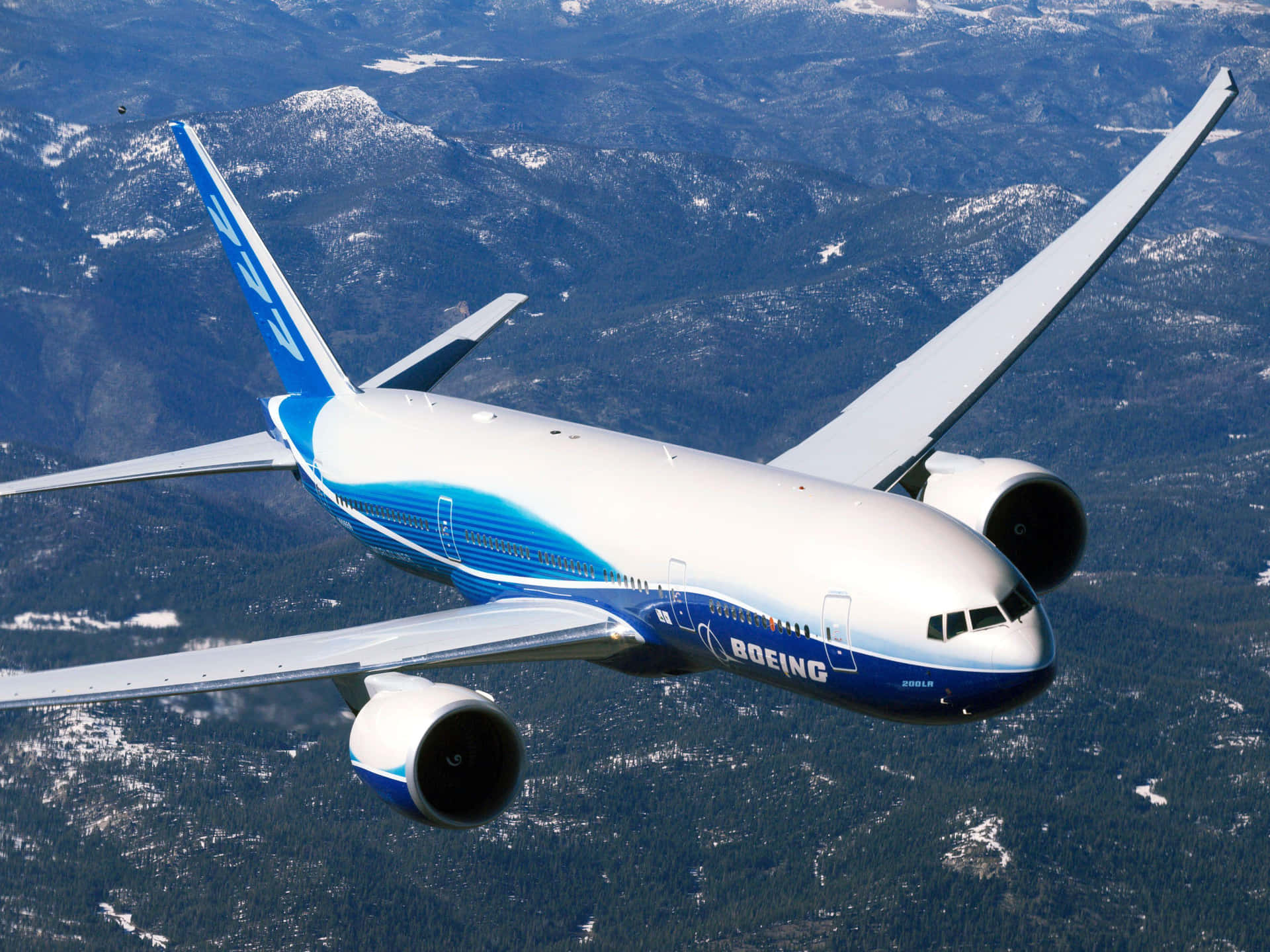 A Blue And White Airplane Flying Over Mountains Background