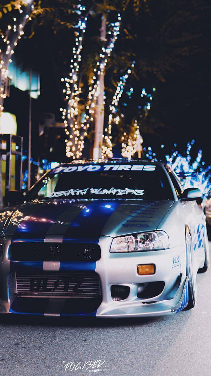 A Blue And White Car Parked In The Street At Night Background