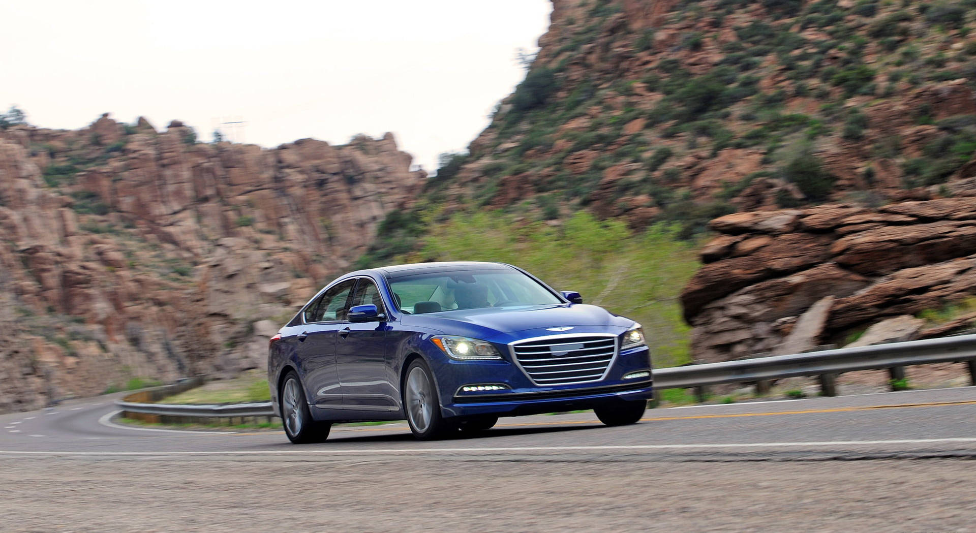 A Blue Car Driving Down A Mountain Road