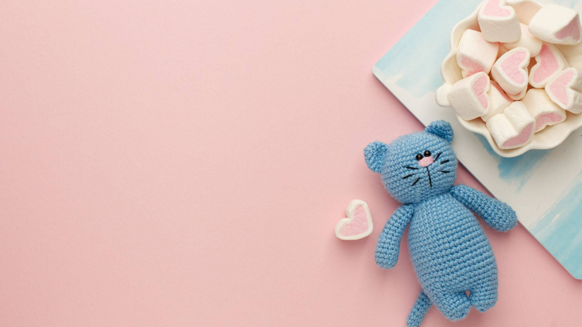 A Blue Crochet Cat With Marshmallows On A Pink Background Background