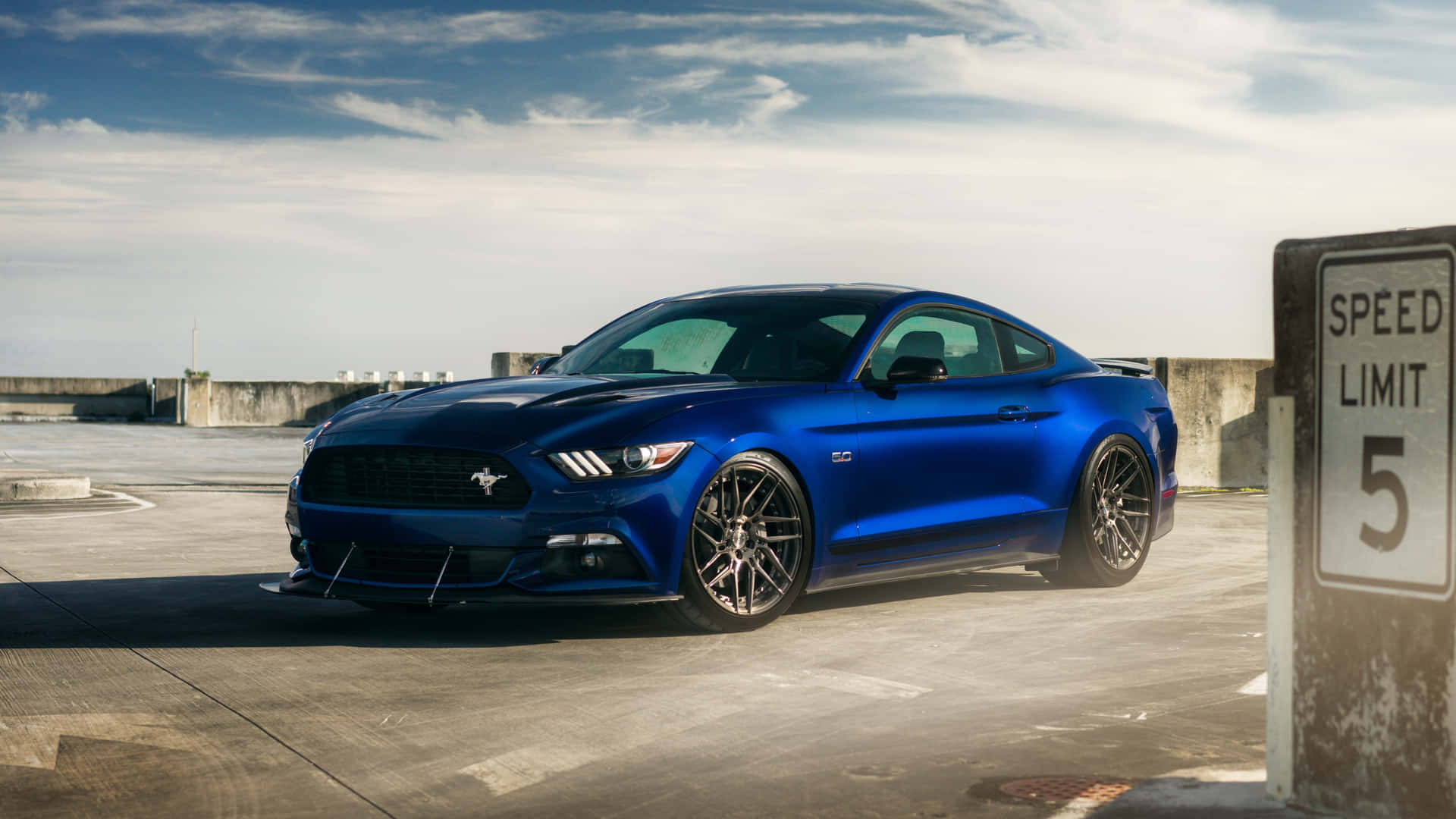 A Blue Ford Mustang Gt Parked In Front Of A Sign Background