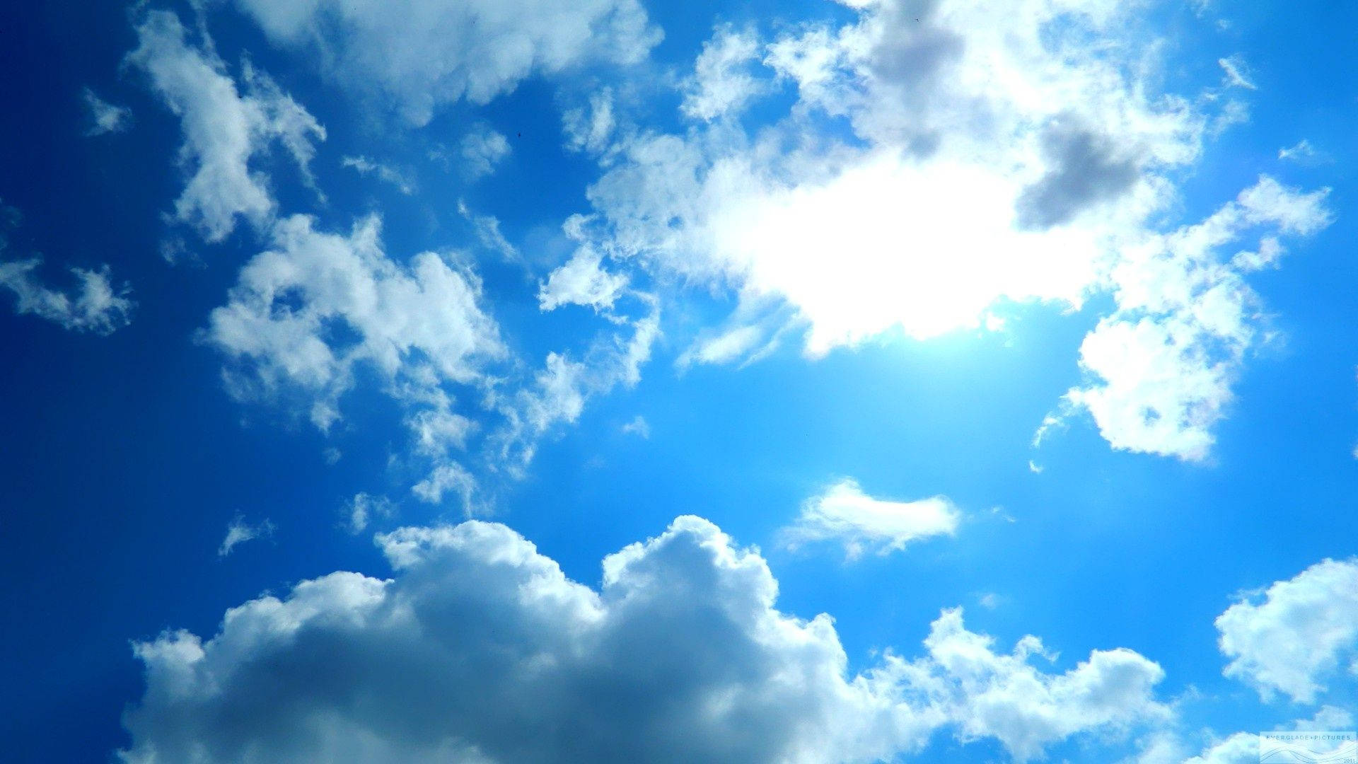 A Blue Sky With Clouds And Sun Background