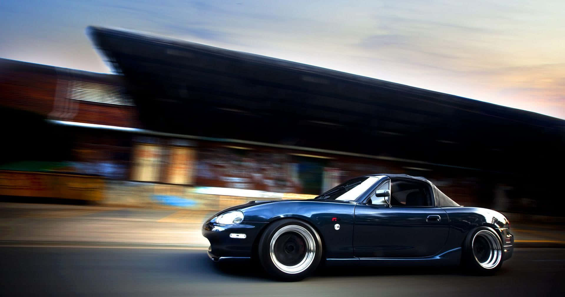 A Blue Sports Car Driving Down The Street Background