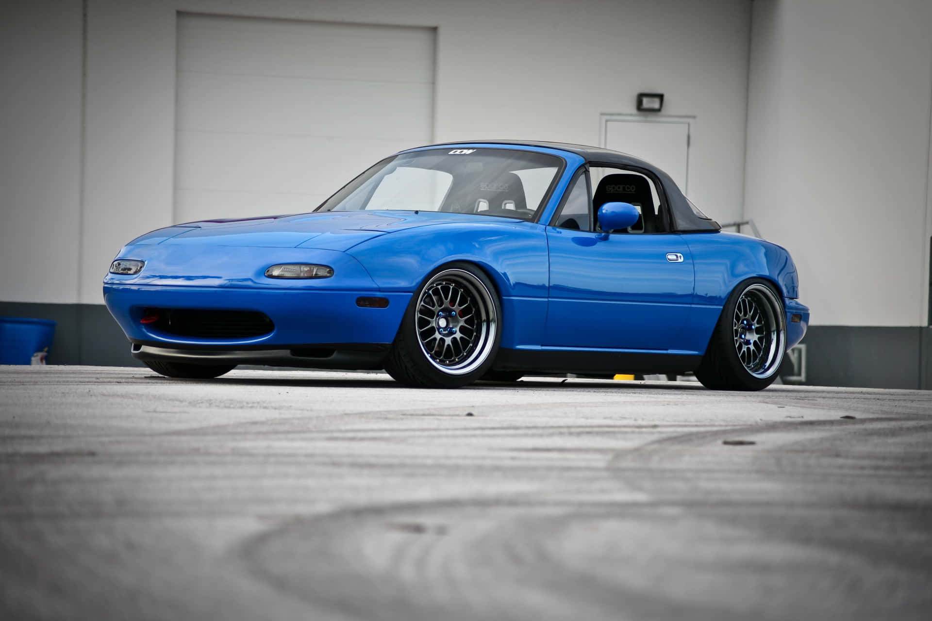 A Blue Sports Car Parked In Front Of A Building Background