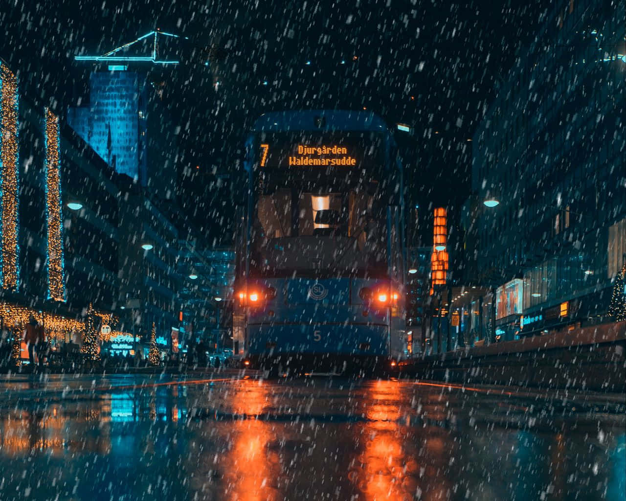 A Blue Tram Driving Down A City Street At Night Background