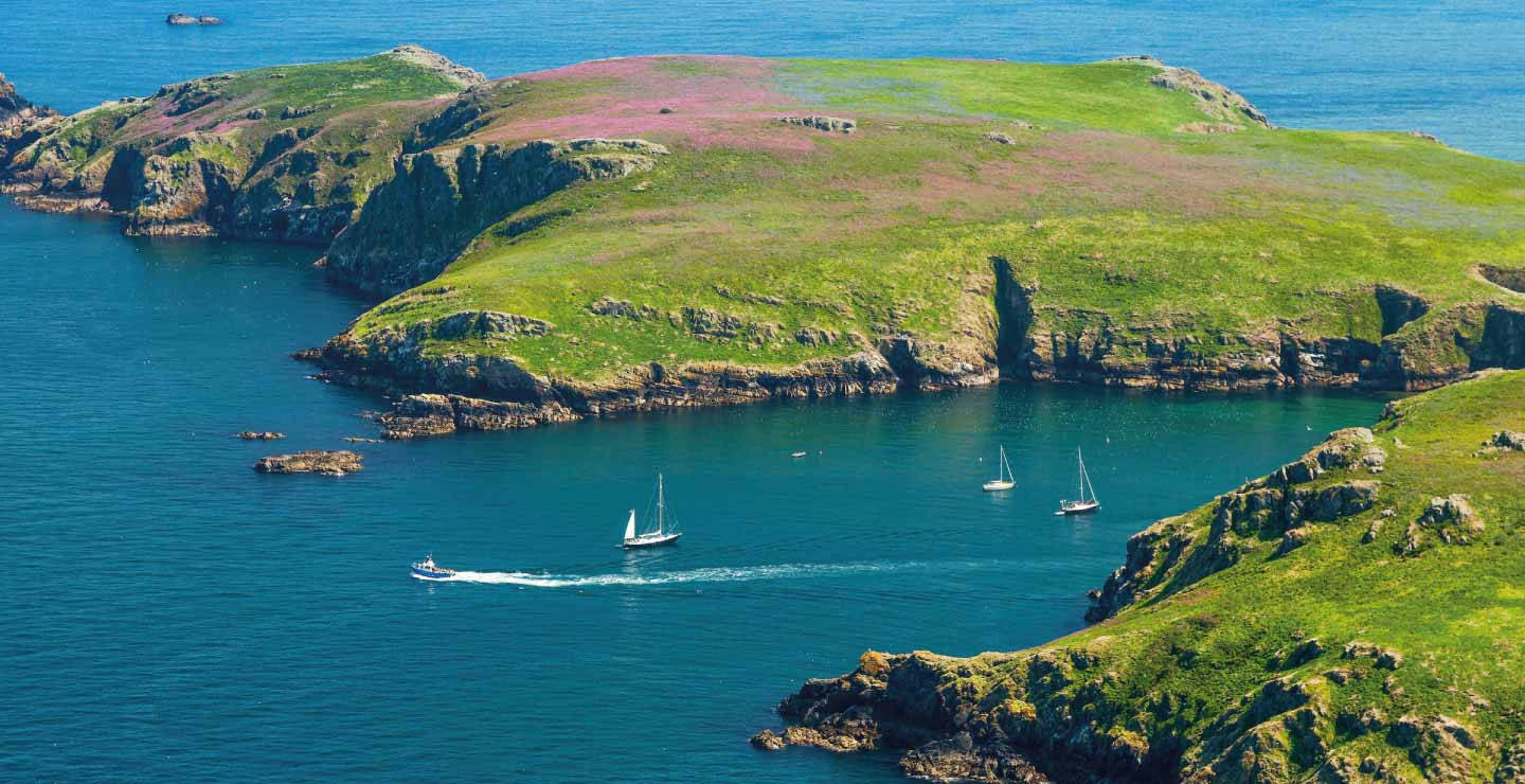 A Boat Is Sailing In The Water Near A Green Island Background