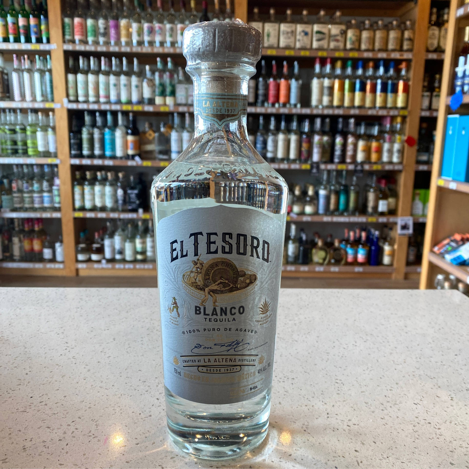 A Bottle Of El Tesoro Blanco Tequila Showcased In A Liquor Shop Background