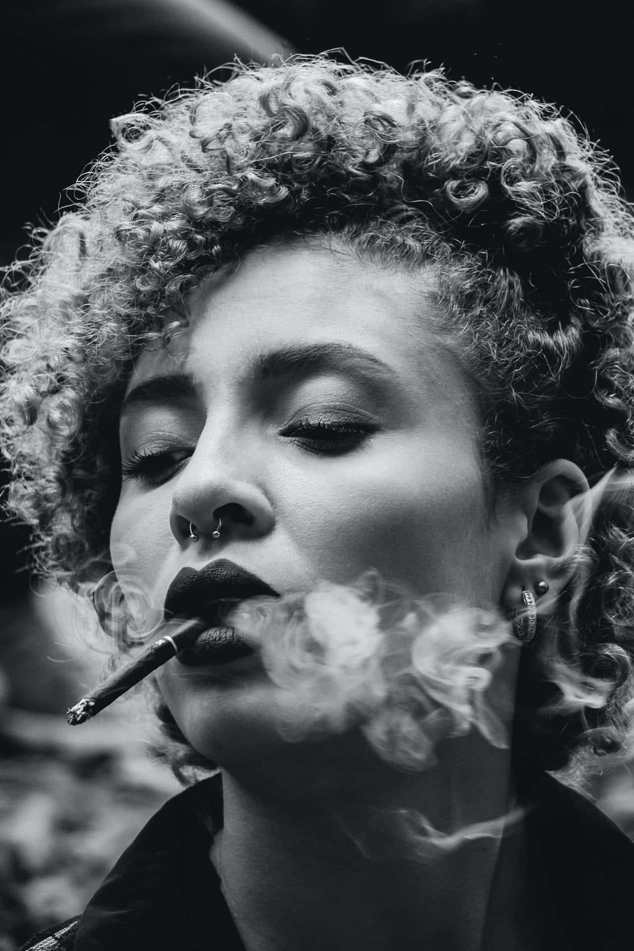 A Carefree Young Woman With Curly Hair Enjoying A Serene Moment With Her Cigarette
