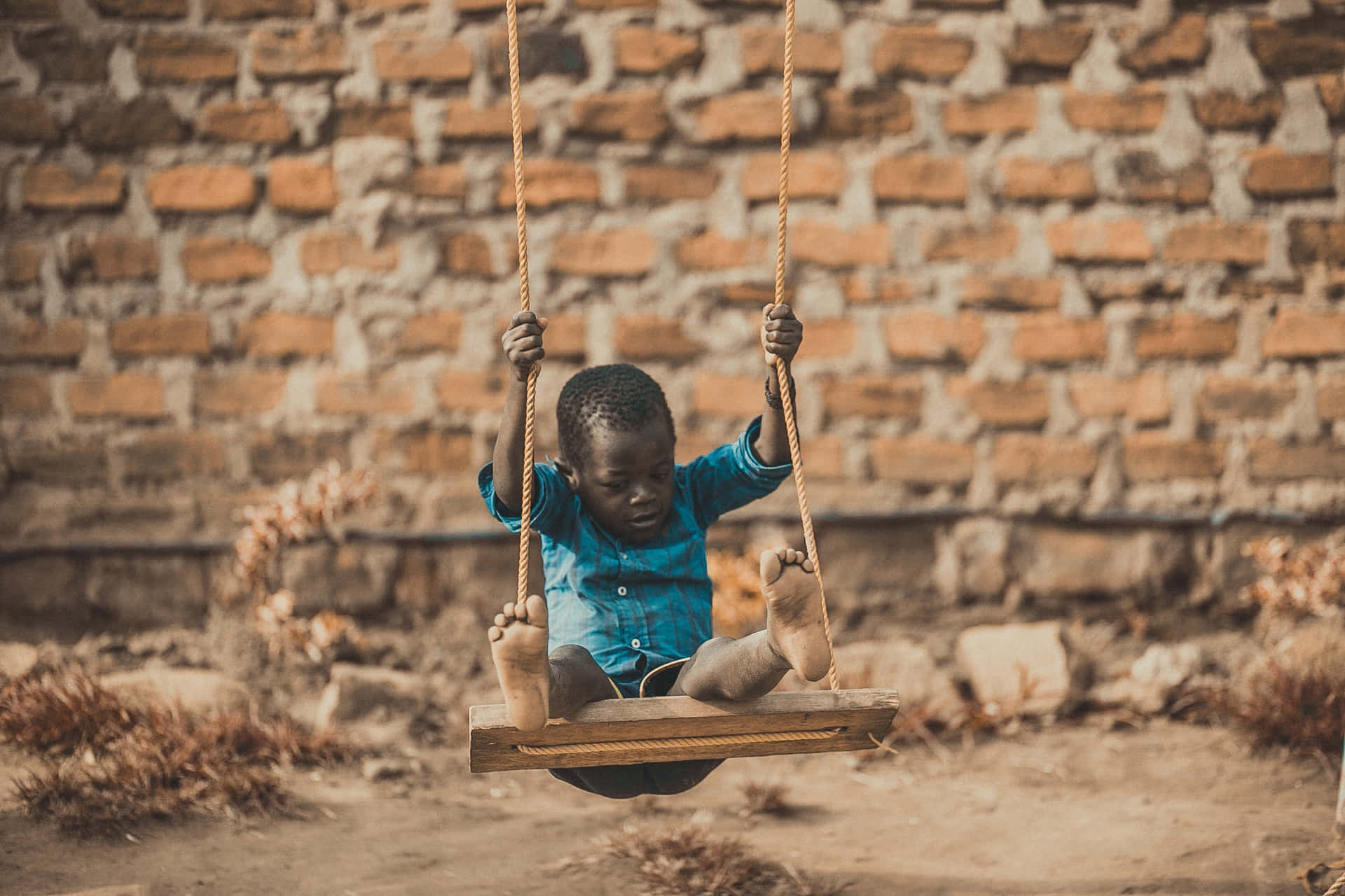 A Child Is Swinging On A Swing In Front Of A Brick Wall Background