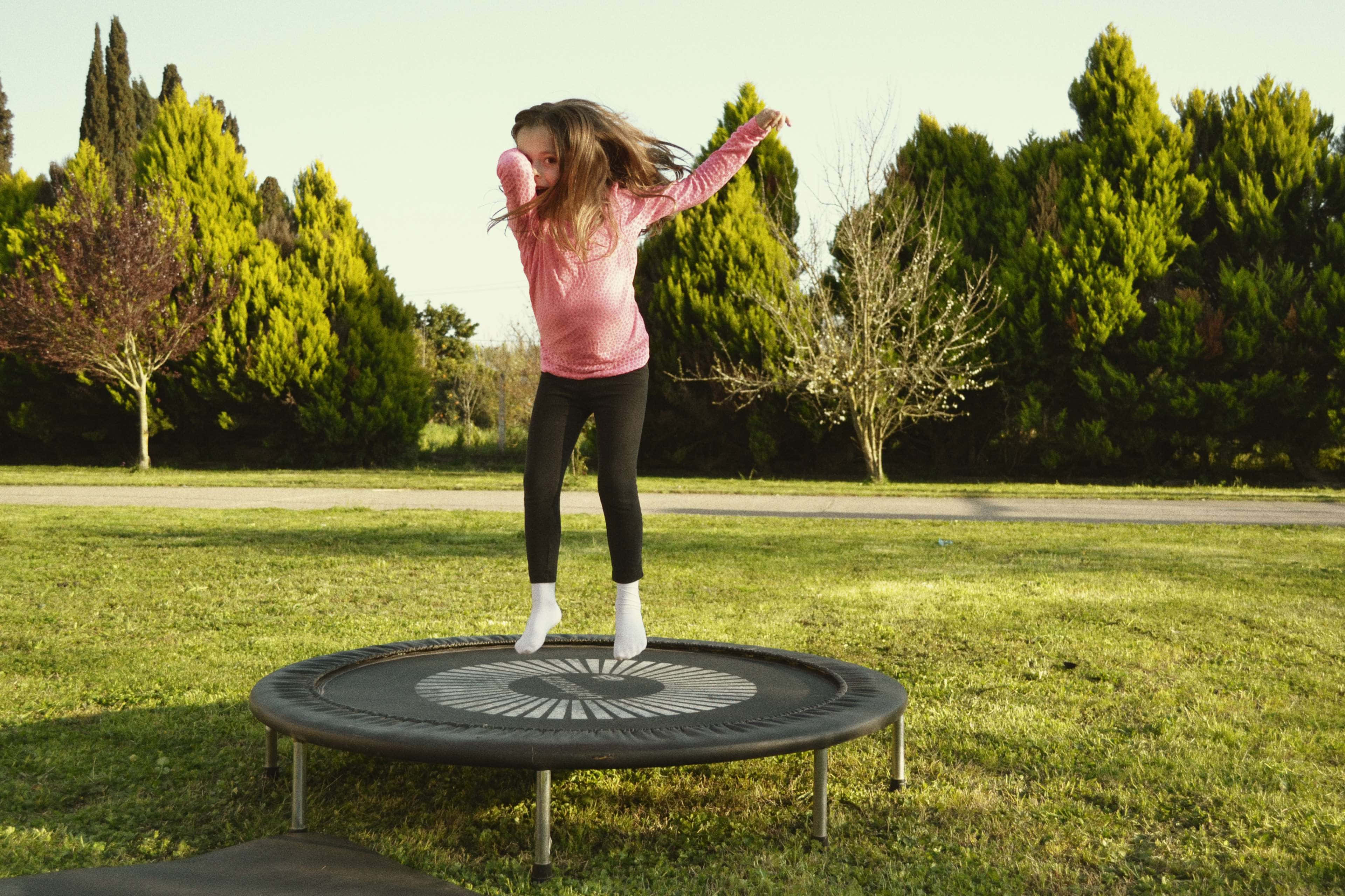 A Child Joyfully Jumping On A Trampoline Under A Bright Sky. Background