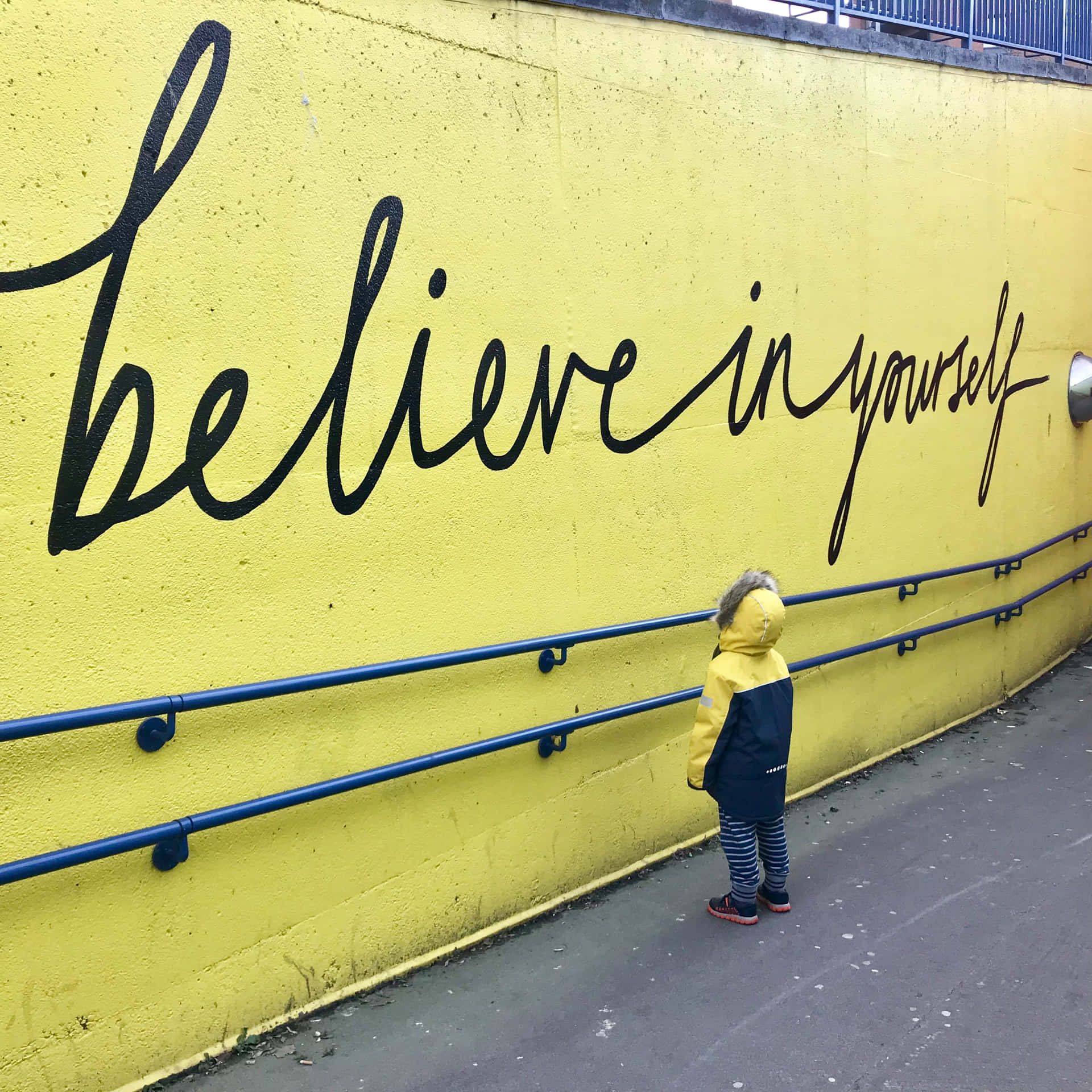 A Child Standing Next To A Yellow Wall With A Quote That Says Believe In Yourself Background
