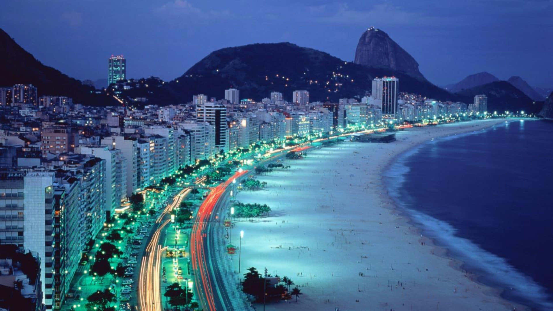 A City At Night With A Beach And Mountains Background