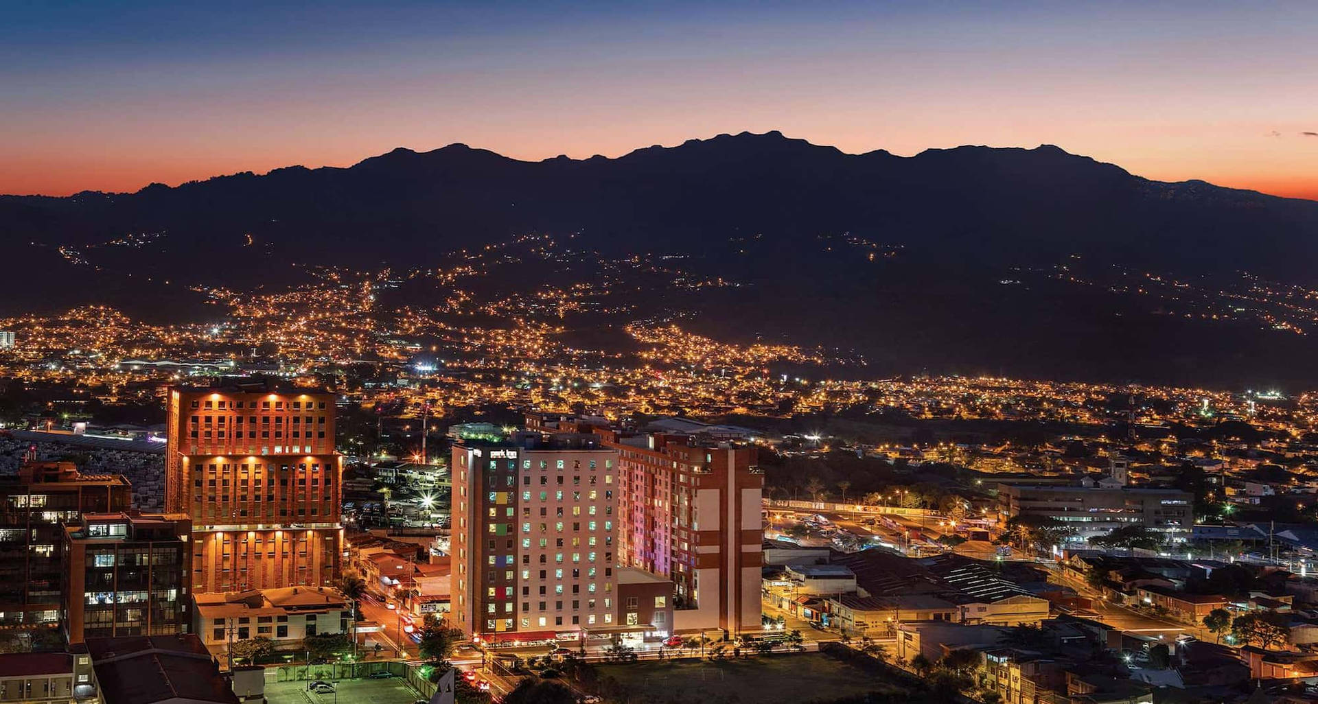 A City At Night With Mountains In The Background Background