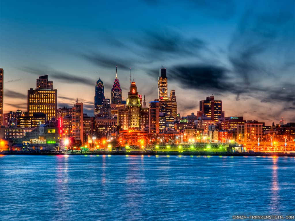 A City Skyline At Night With Lights On The Water Background