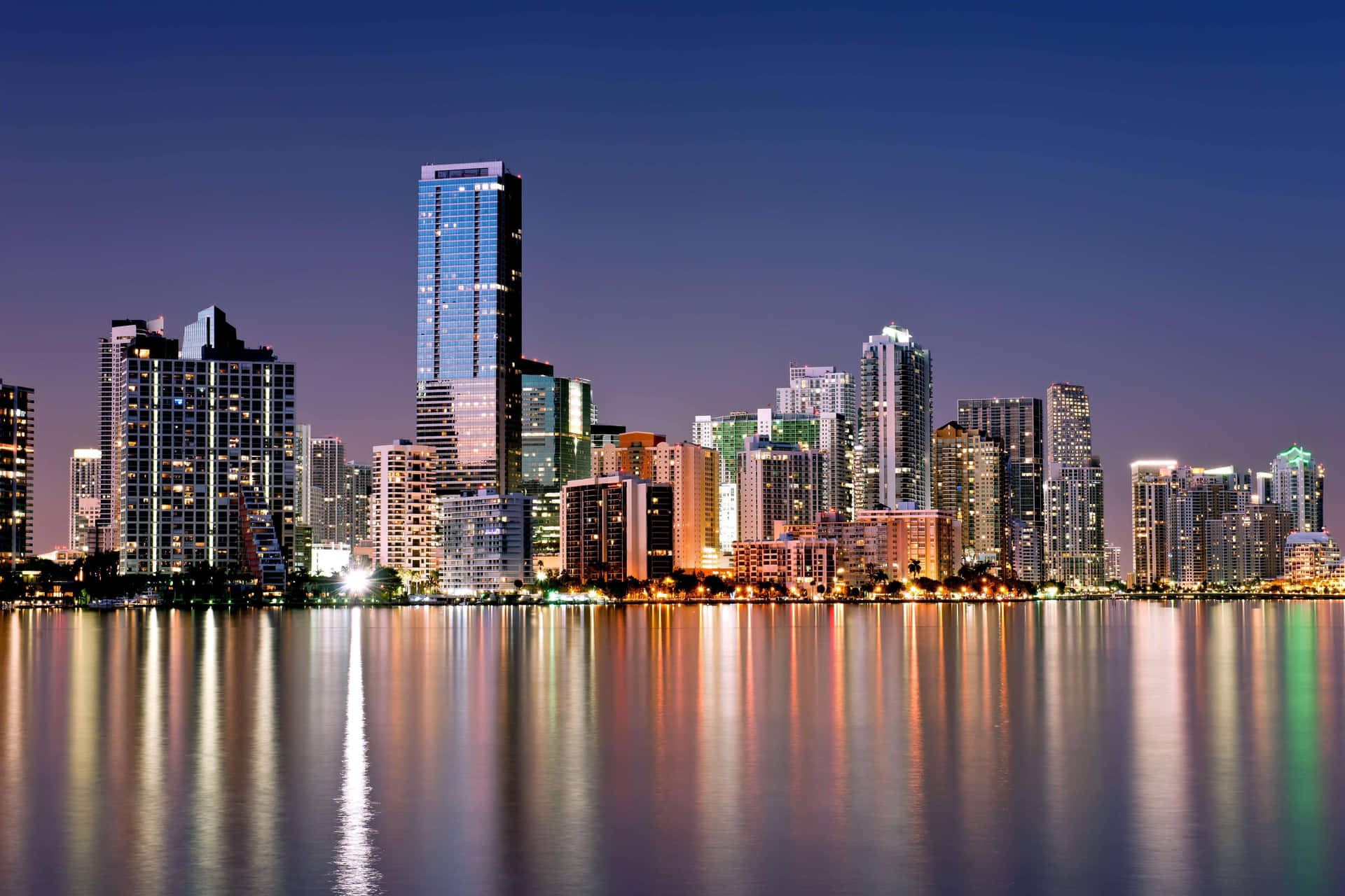 A City Skyline Is Reflected In The Water At Night Background