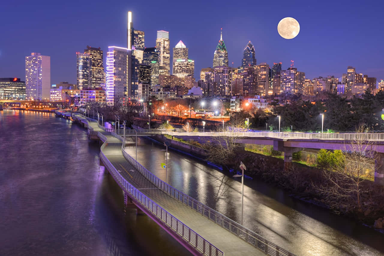 A City Skyline With A Full Moon Over A River Background