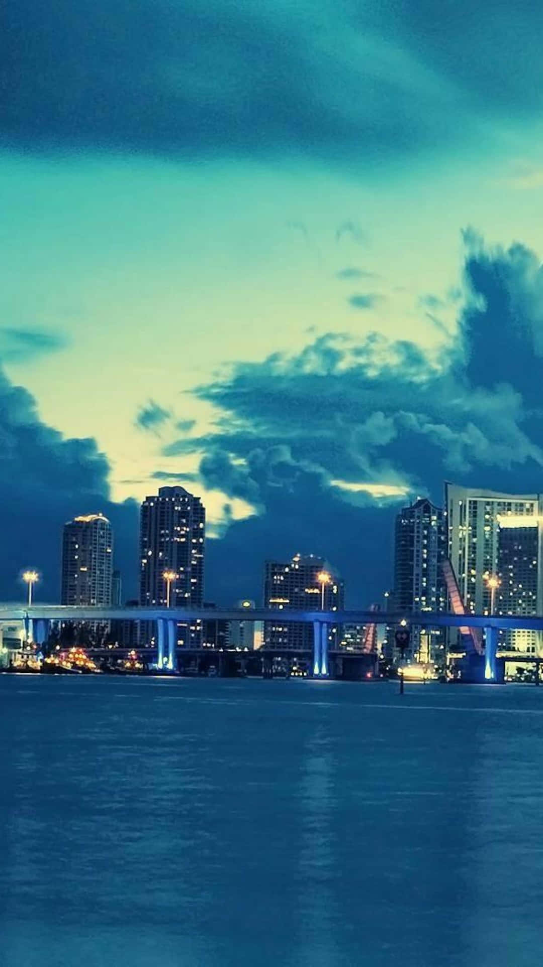 A City Skyline With Clouds Over The Water Background