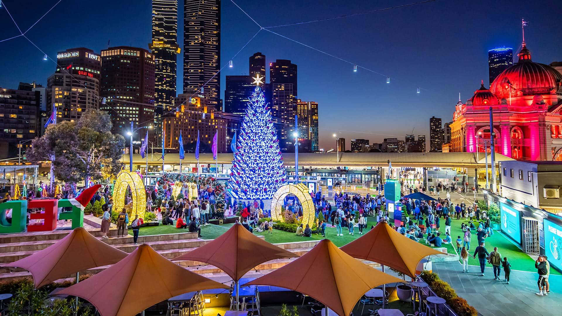 A City With A Christmas Tree And People In The Middle Background