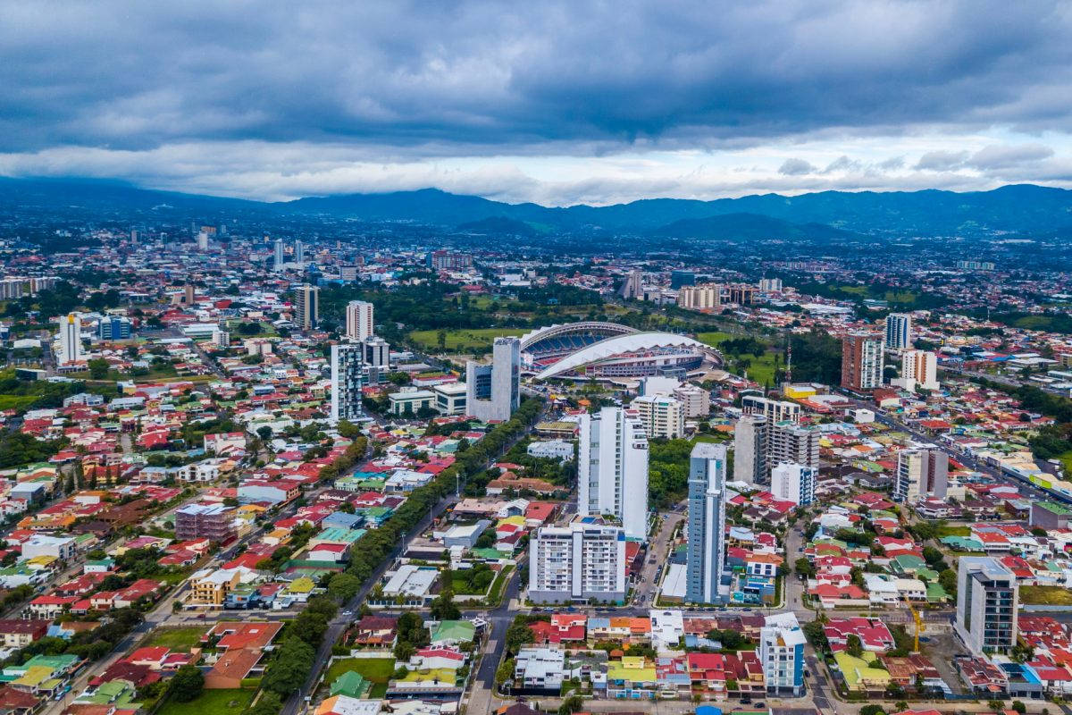 A City With A Stadium And Mountains In The Background Background