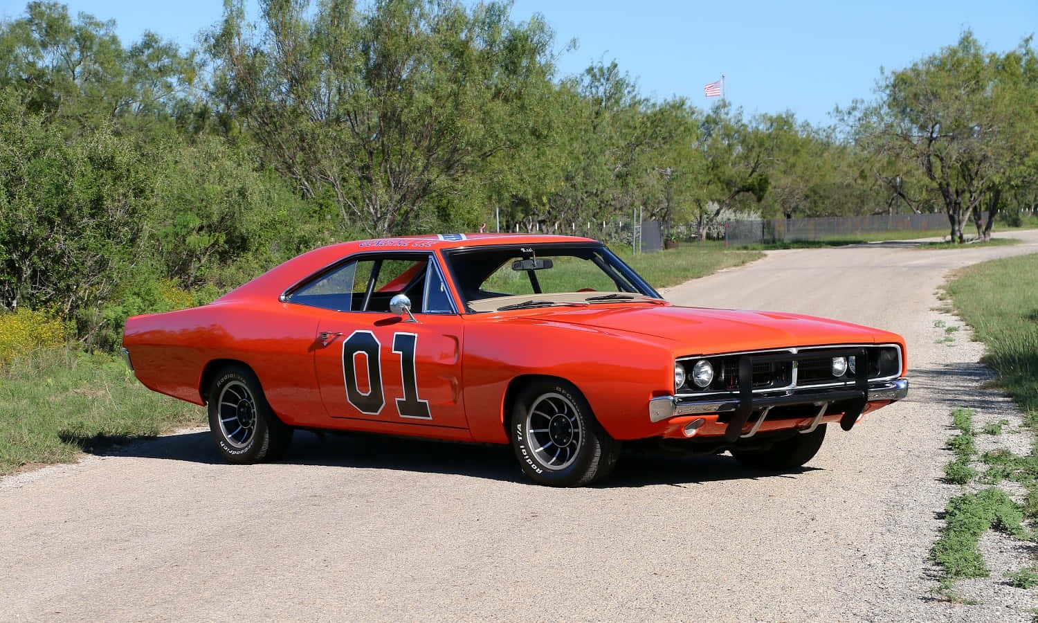 A Classic Orange Muscle Car Is Driving Down A Dirt Road Background