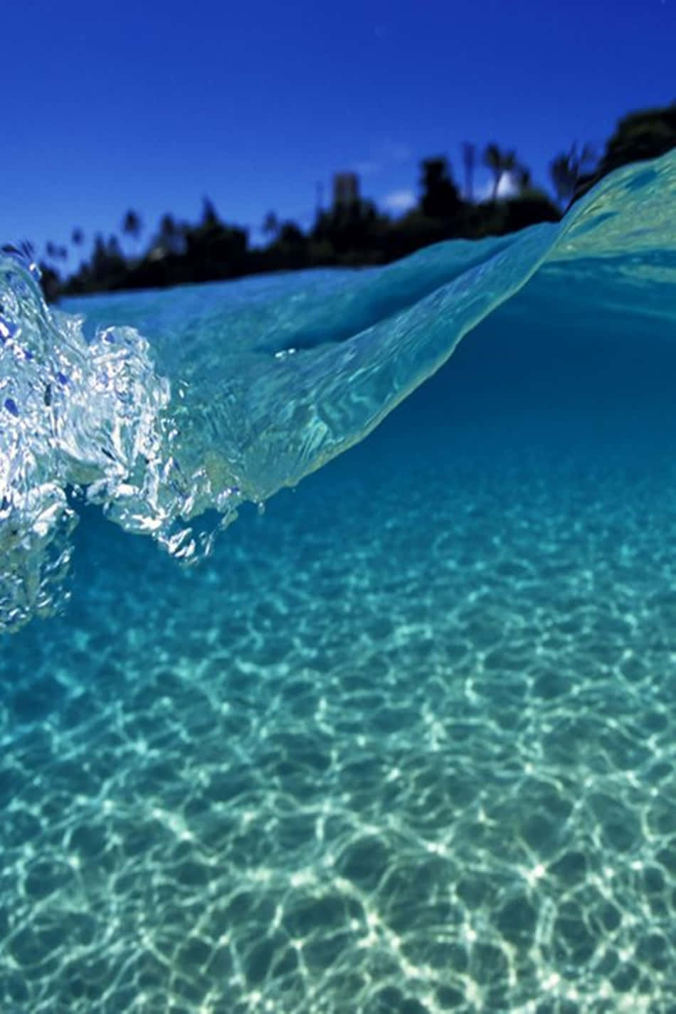 A Clear Blue Ocean With A Wave In The Background Background