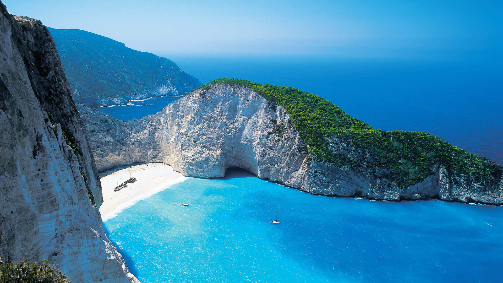 A Cliff With Blue Water And A Beach Background