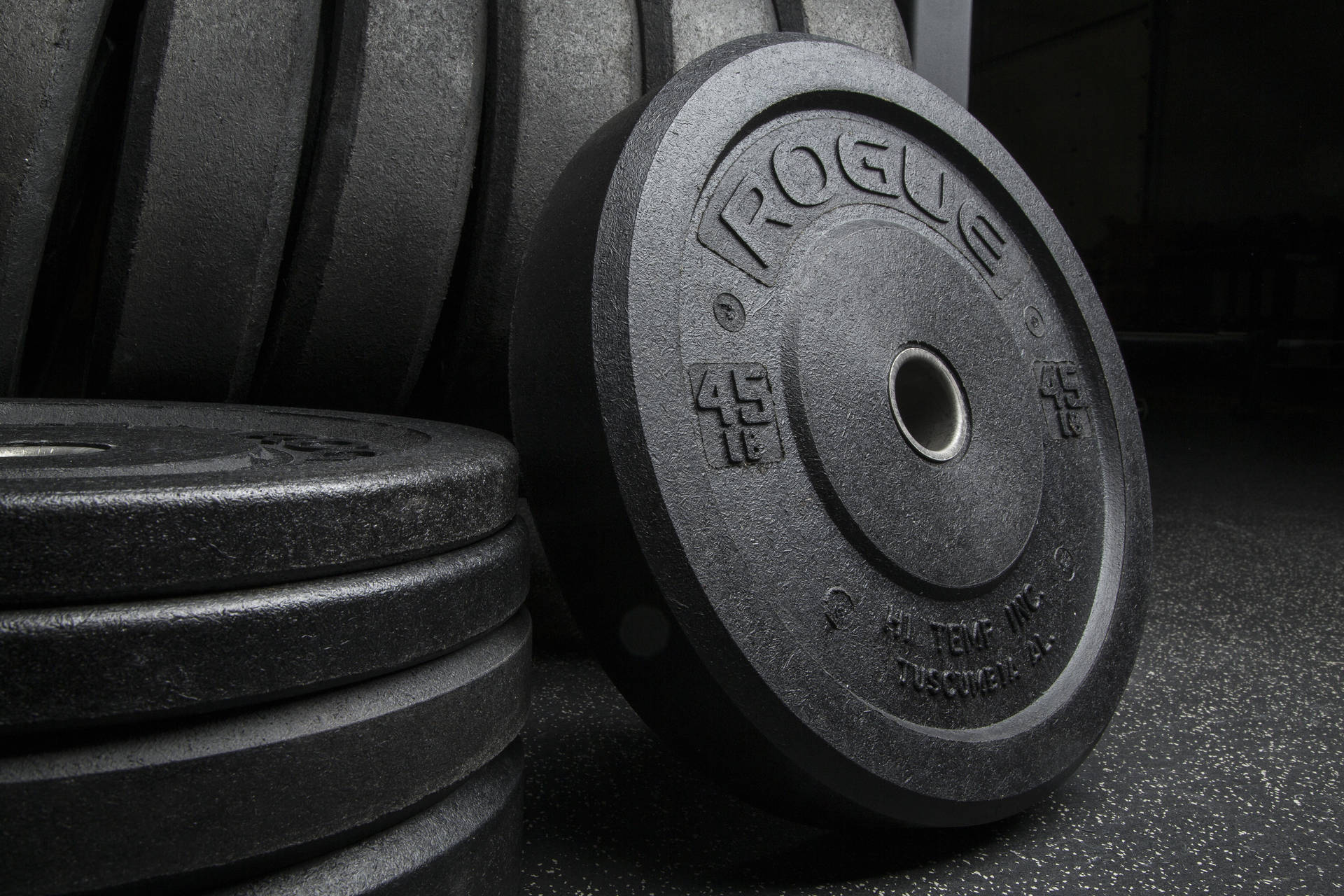 A Close-up Shot Of Rogue Barbell Plates Stacked Diligently On A Rack Background