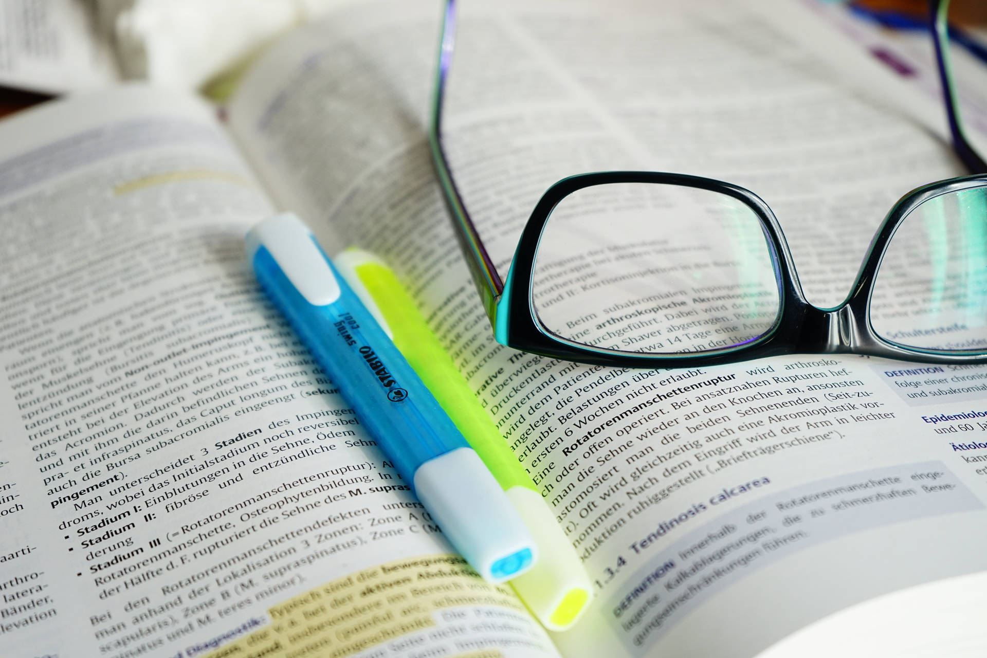 A Close-up View Of Reference Book, Highlighters, And Eyeglasses